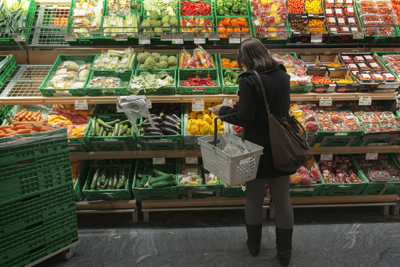 Una donna mentre fa la spesa davanti al banco delle verdure.
