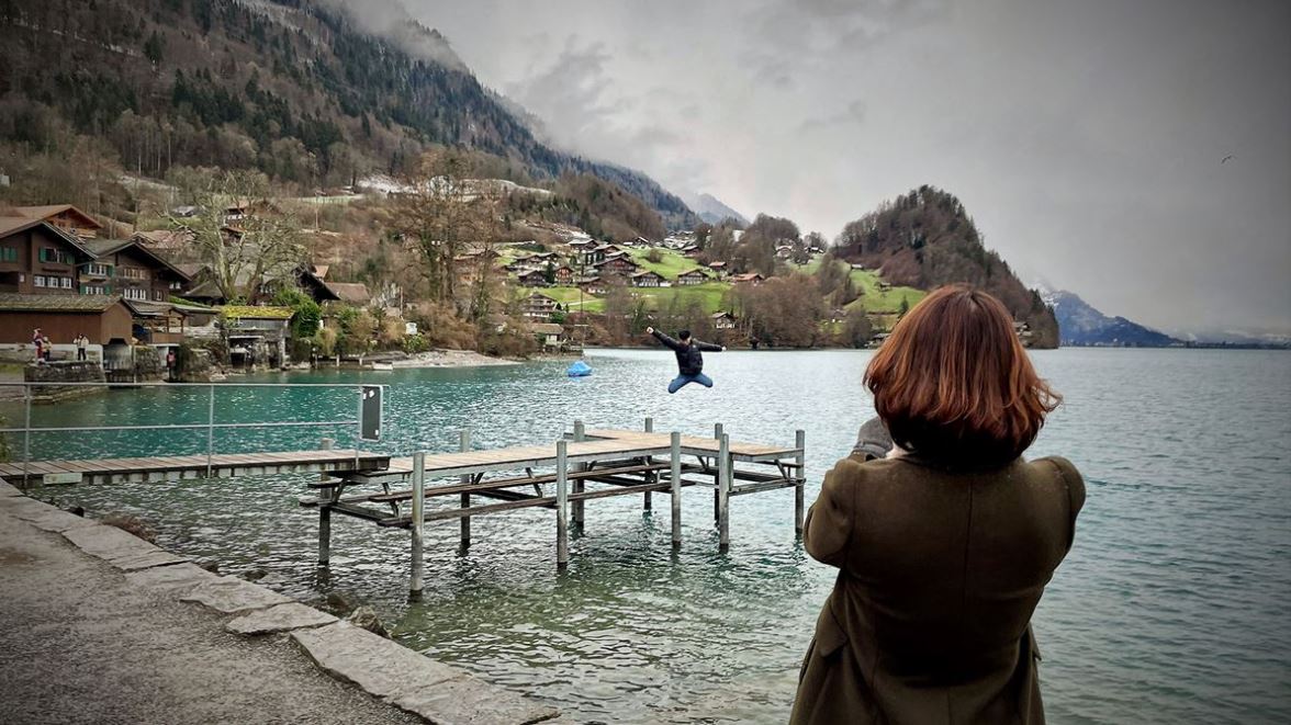 Frau fotografiert eine Person, die auf dem Holzsteg im Brienzersee bei Iseltwald einen Luftsprung macht