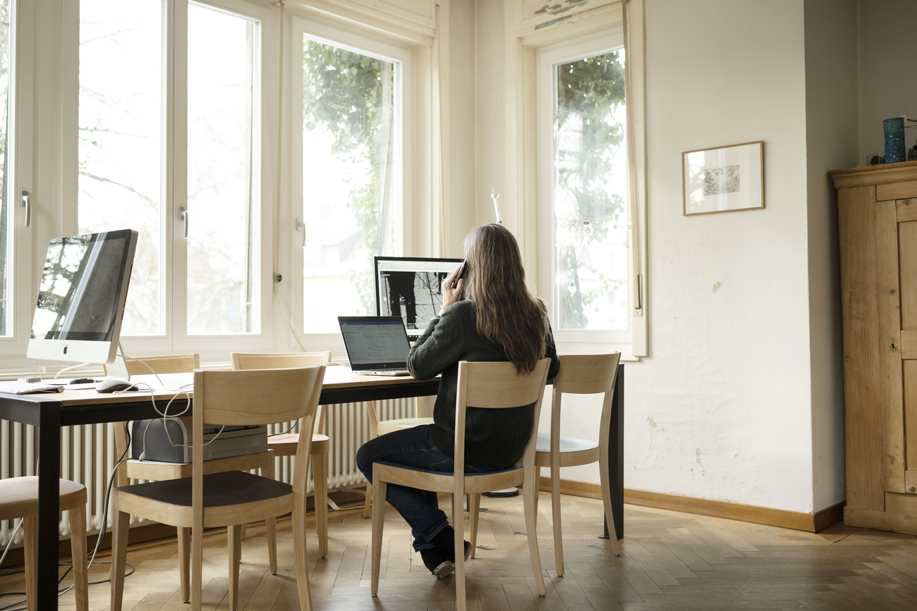 Una donna di spalle davanti al suo Pc mentre parla al telefono.