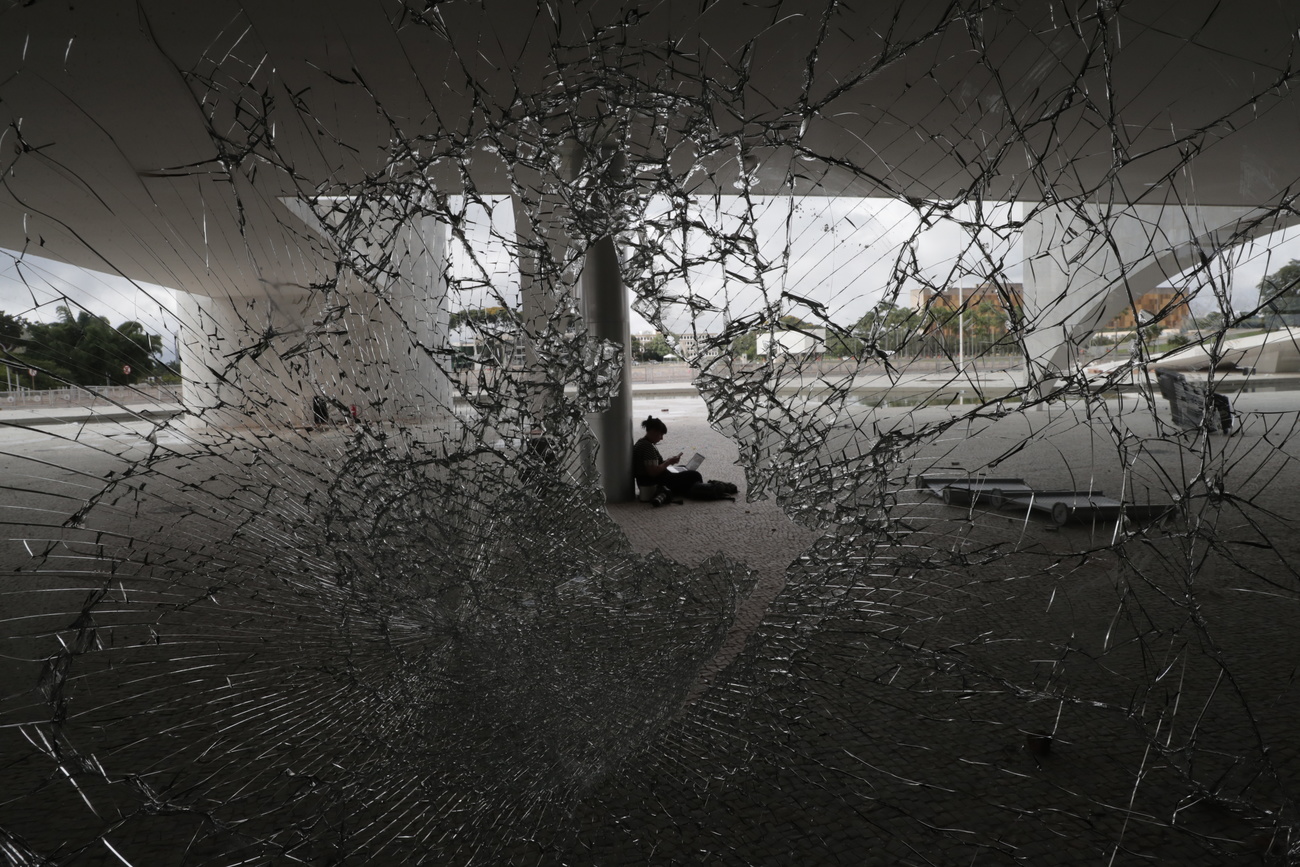 Una persona sentada tras la ventana destrozada del edificio del Congreso de Brasil.