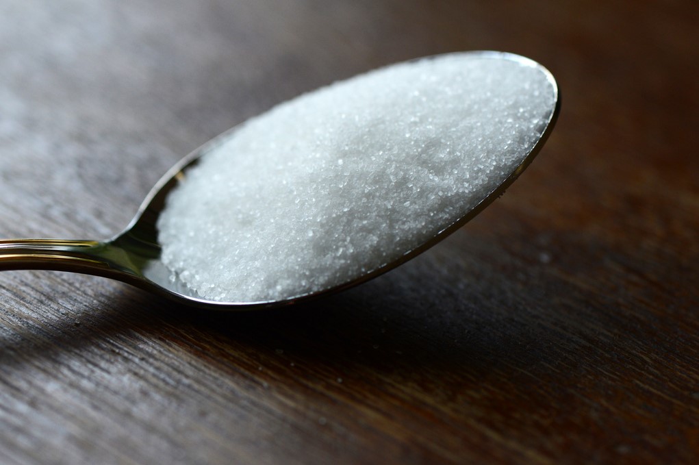 cucchiaio riempito di zucchero appoggiato su una superficie in legno