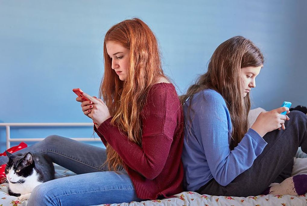 zwei Mädchen Rücken an Rücken, die auf dem Handy tippen