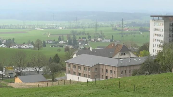 Häuser vor grüner Landschaft mit leichtem Dunst