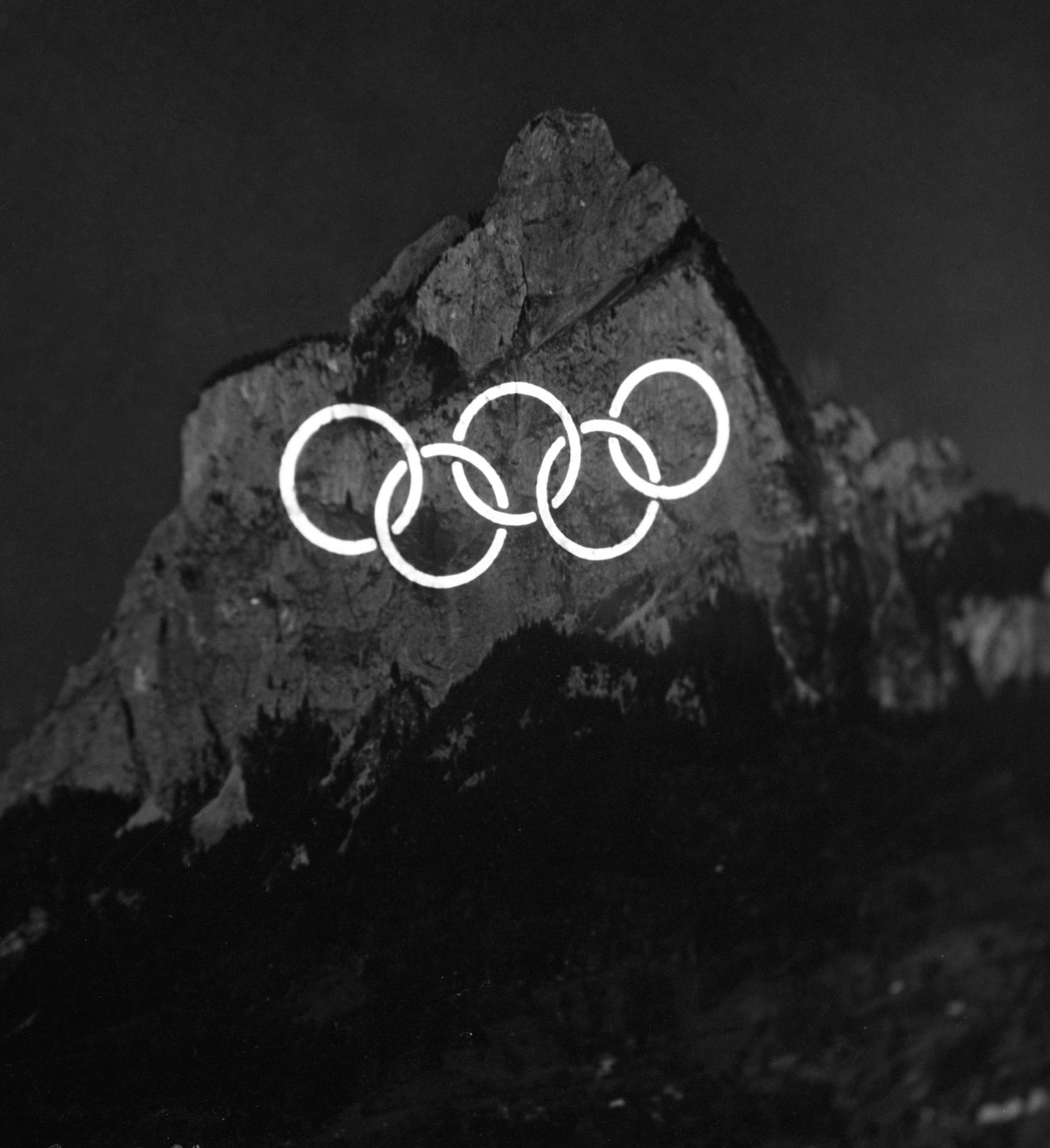 The Olympic logo projected on a mountain face. Picture in black/white