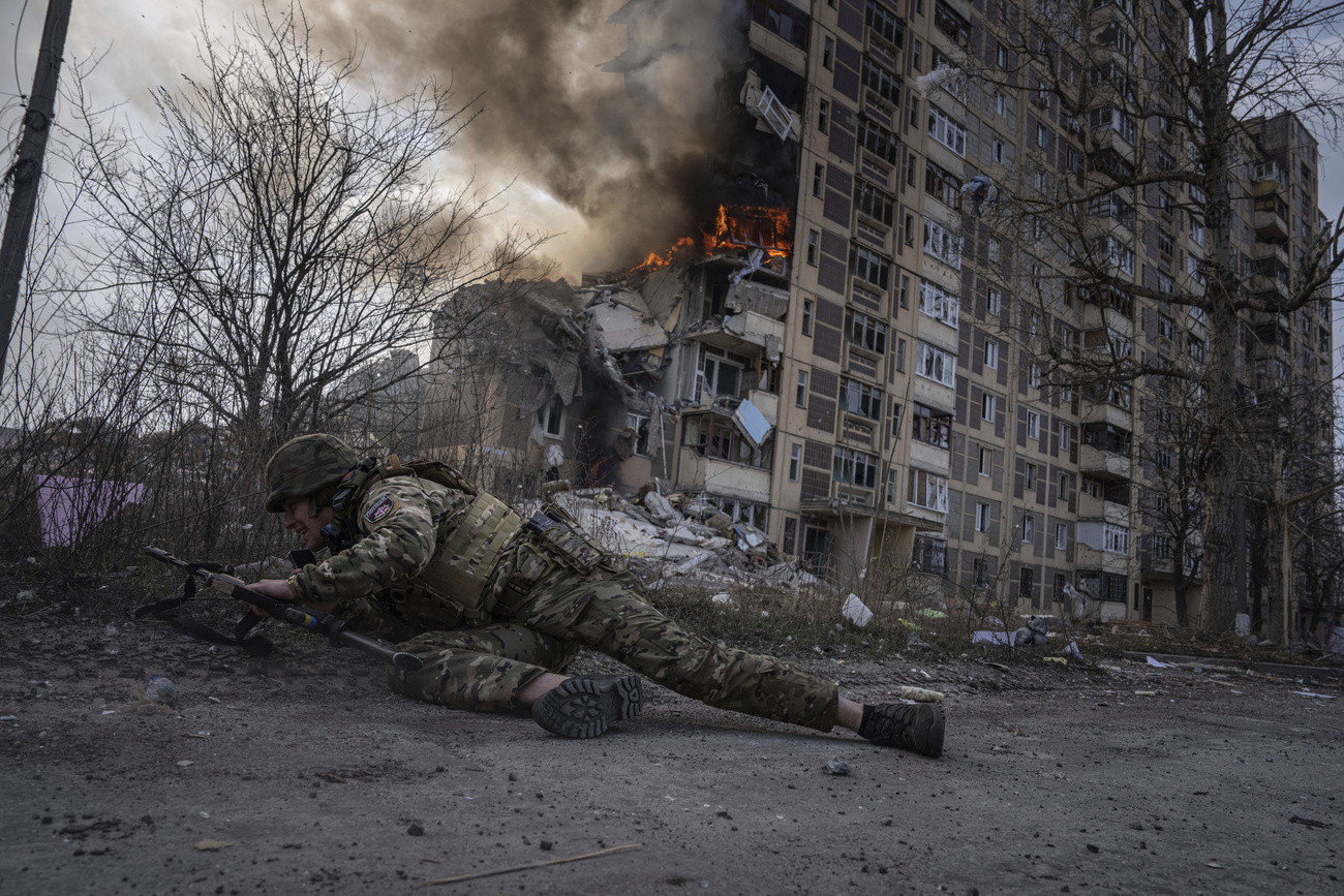 جندي أوكراني يختبئ وفي الخلفية آثار قصف لبناية سكنية