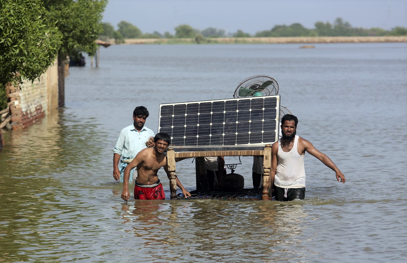 tre uomini trasportano un pannello solare in una zona inondata