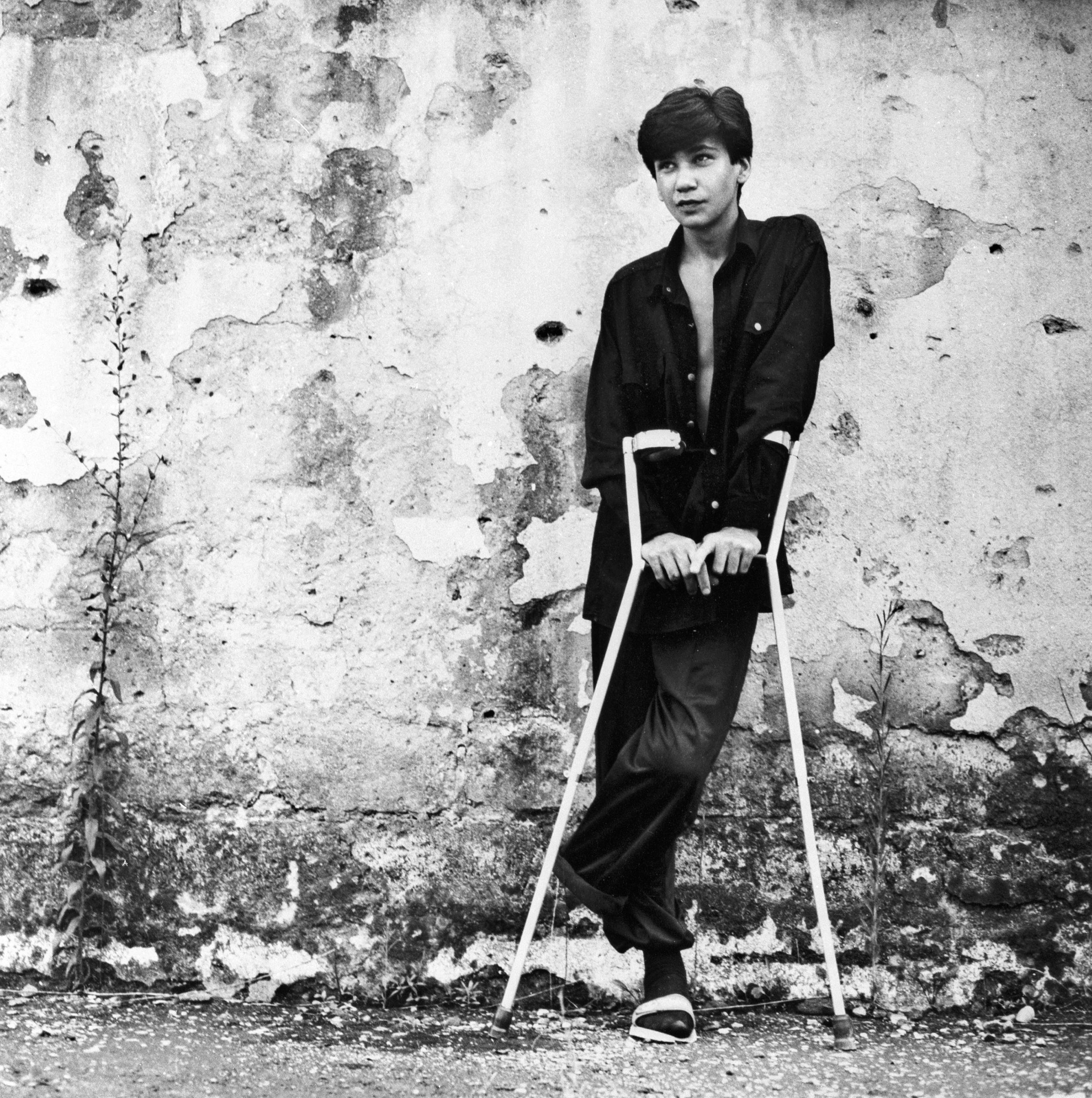 Black and white picture of a young boy with crutches in front of a wall.