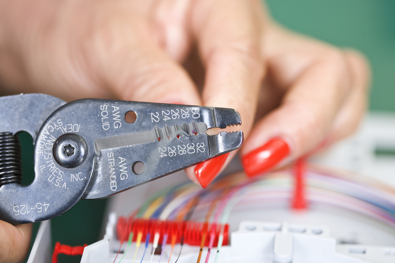primo piano di mani di donna con unghie rosse che lavorano con una tenaglia