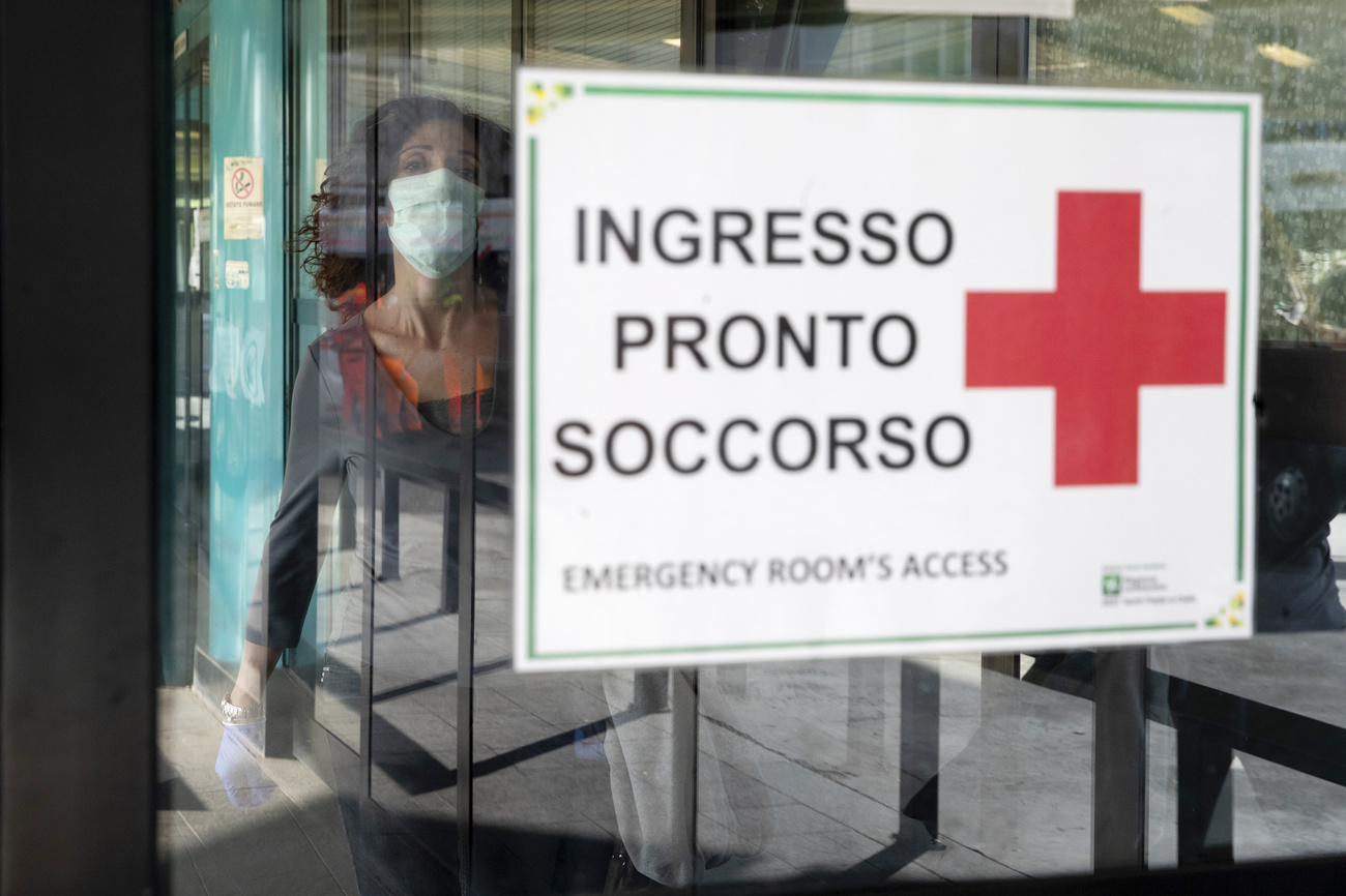 vetro con cartello INGRESSO PRONTO SOCCORSO. dietro al vetro una donna con mascherina chirurgica