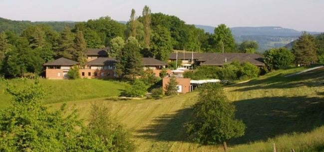 Rote Backsteingebäude inmitten vieler Bäume und grüner Hügel