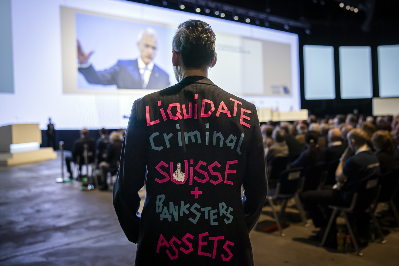 Ein Mann im Anzug mit der Aufschrift Liquidate criminal suisse + banksters assets