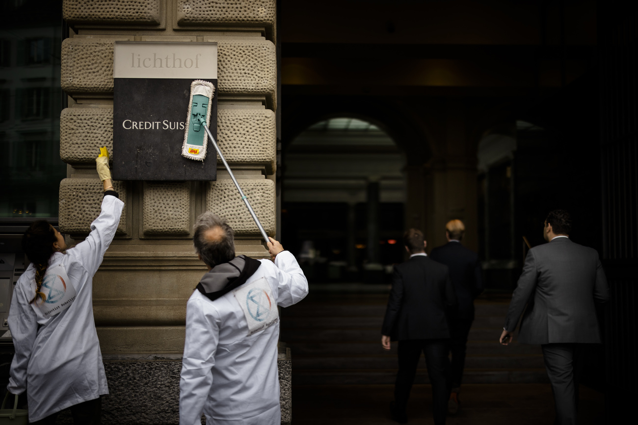 Photo of two protesters symbolically clearing Credit Suisse sign