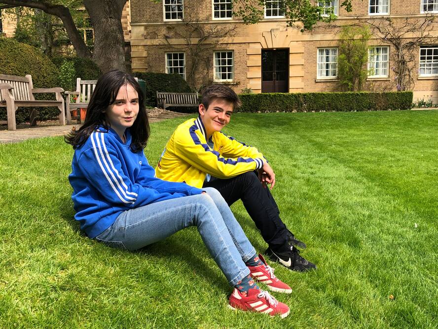 Ada (11) and Ruben (13) live with their parents and older brother in Cambridge (UK). The siblings sit on a green lawn.
