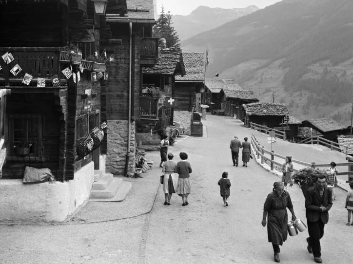 Black and white photo of a mountain village with wooden houses and people on the street
