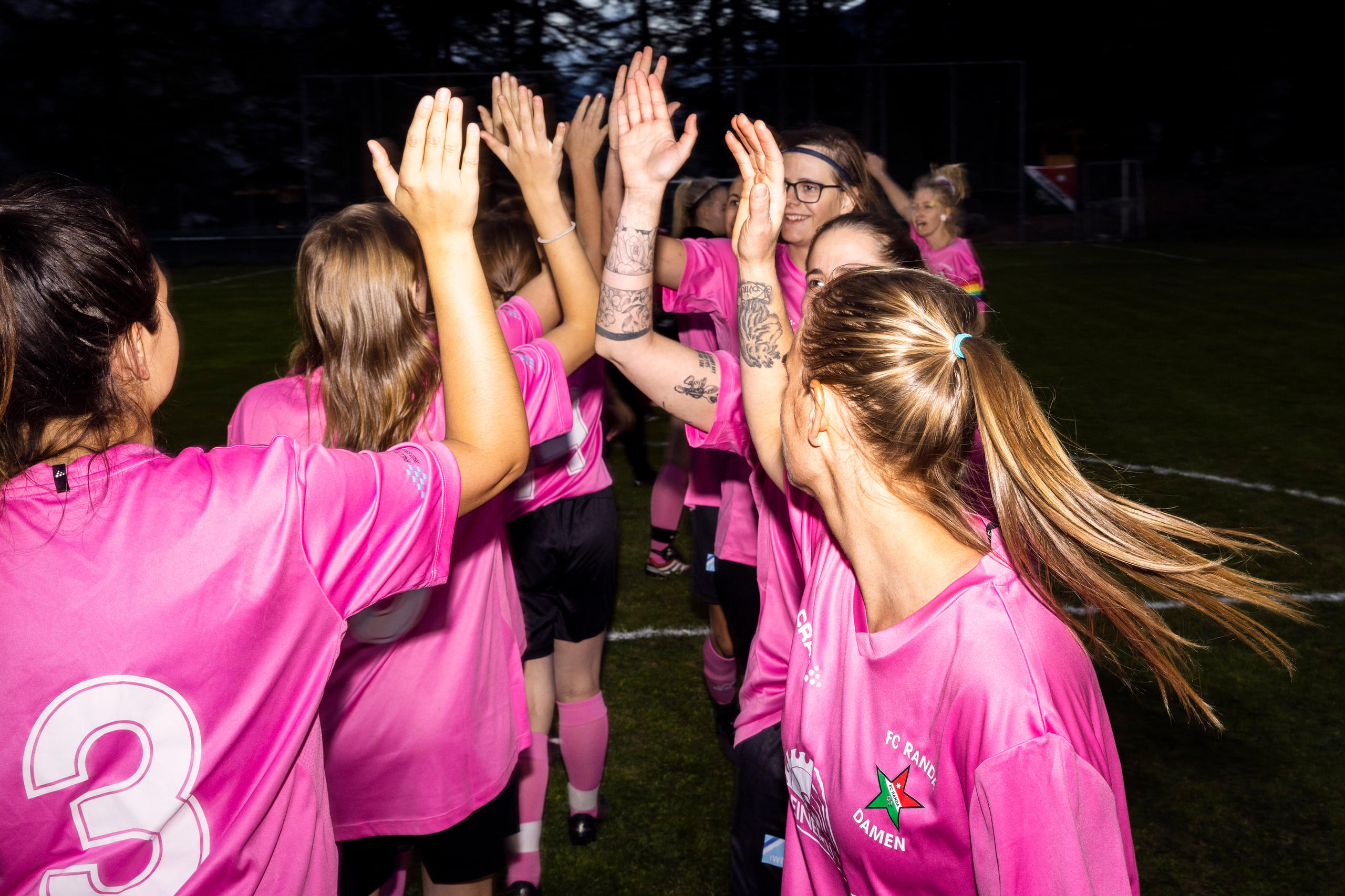 A group of people high-fiving dressed in numbered pink shirts