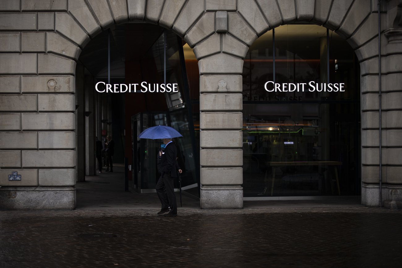 Une personne marche devant Credit Suisse à Zurich un jour de pluie.