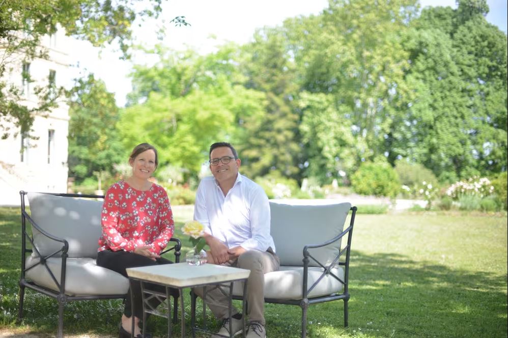 A man and woman sit and pose for a photo. They are a Swiss couple who have moved abroad to France.