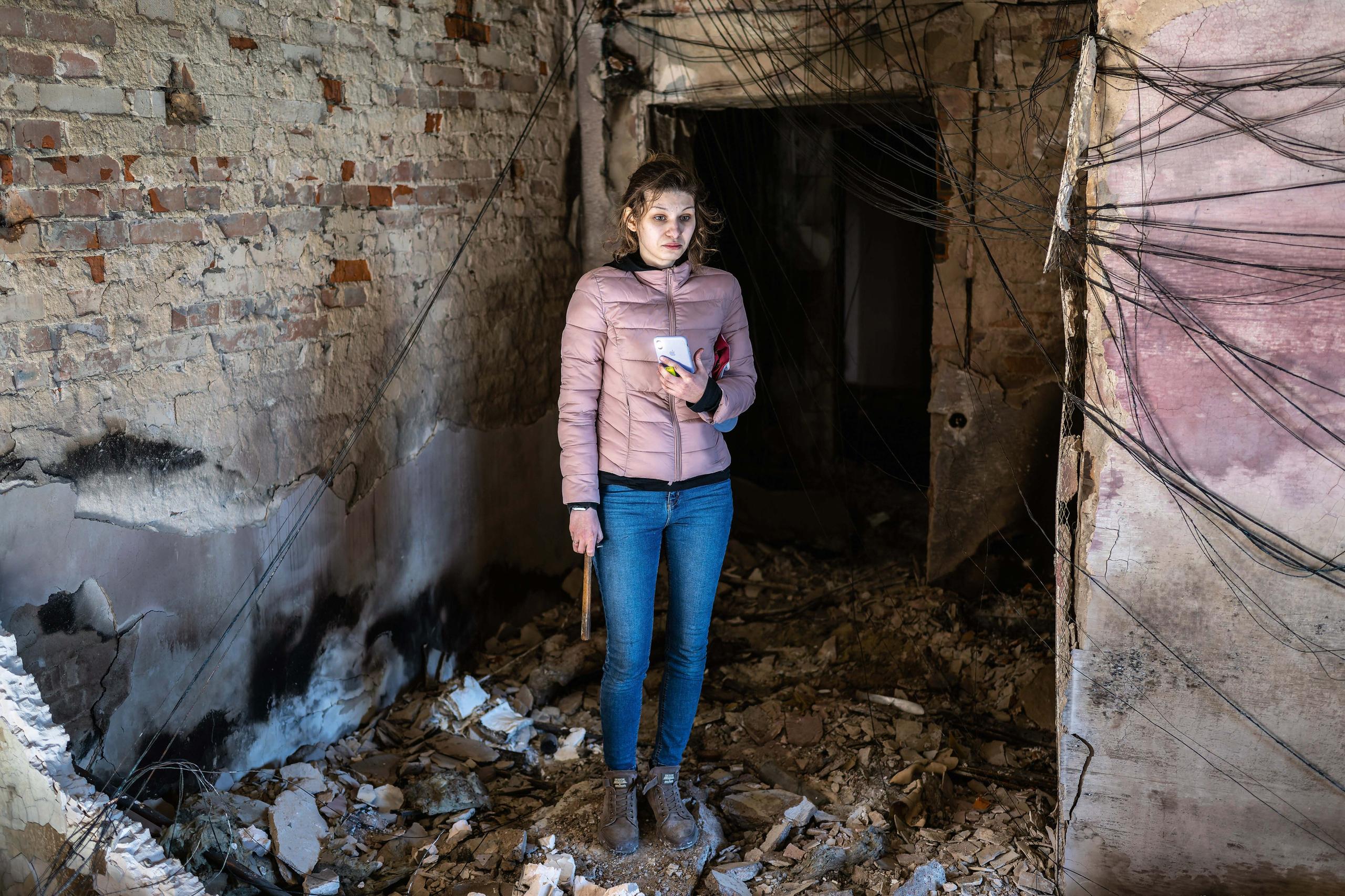 A person wearing a pink Jacket stands within the rubble of a destroyed building in Ukraine