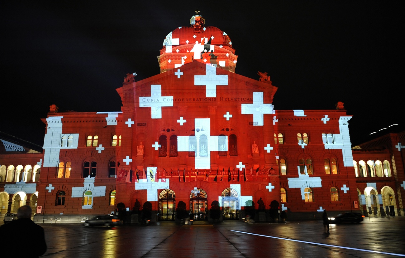 Palazzo federale ricoperto di bandiere della Svizzera in un gioco di luci.