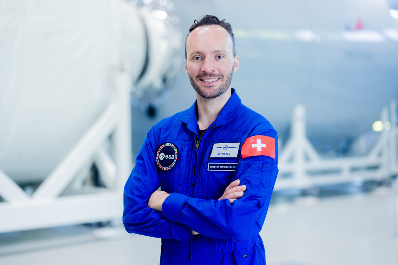 Marco Sieber in an astronaut training suit in front of a 1:1 model of an ISS module. The Swiss flag prominently on his shoulder