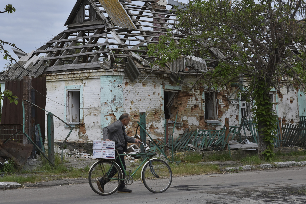 Man with bicycle and humanitarian aid in front of destroyed house in Ukraine.