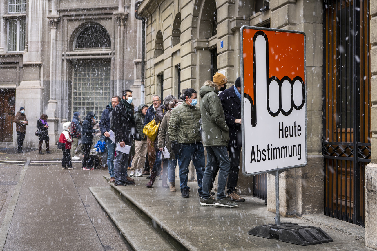 Des gens portant des masques devant un bureau de vote