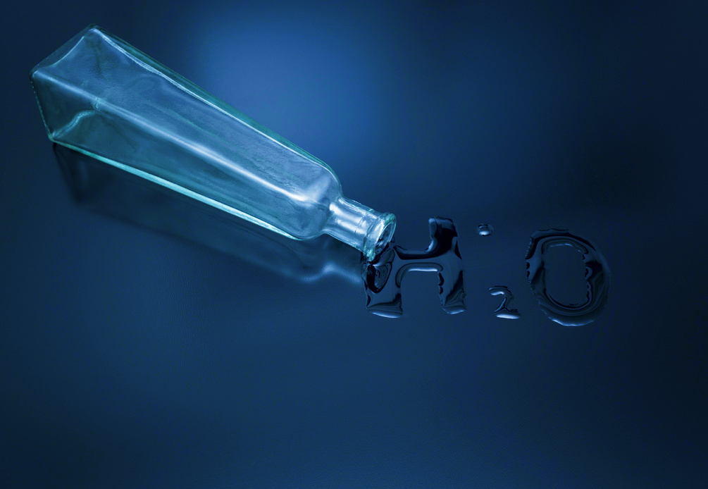 bottiglia vuota rovesciata da cui è fuoriuscita dell acqua che va a formare la scritta h due o