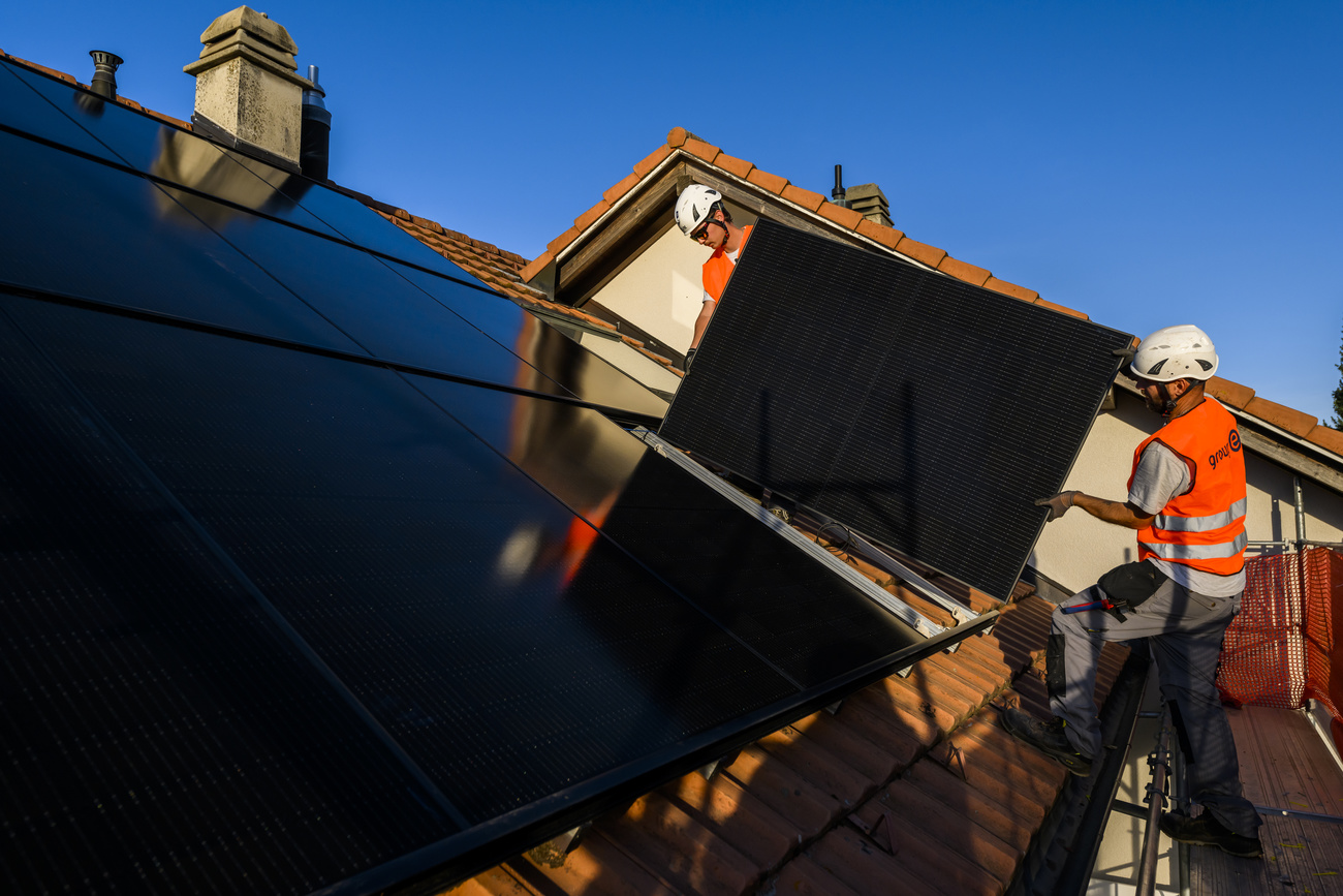 عمال يضعون ألواحًا شمسية على سطح أحد المباني في سويسرا.