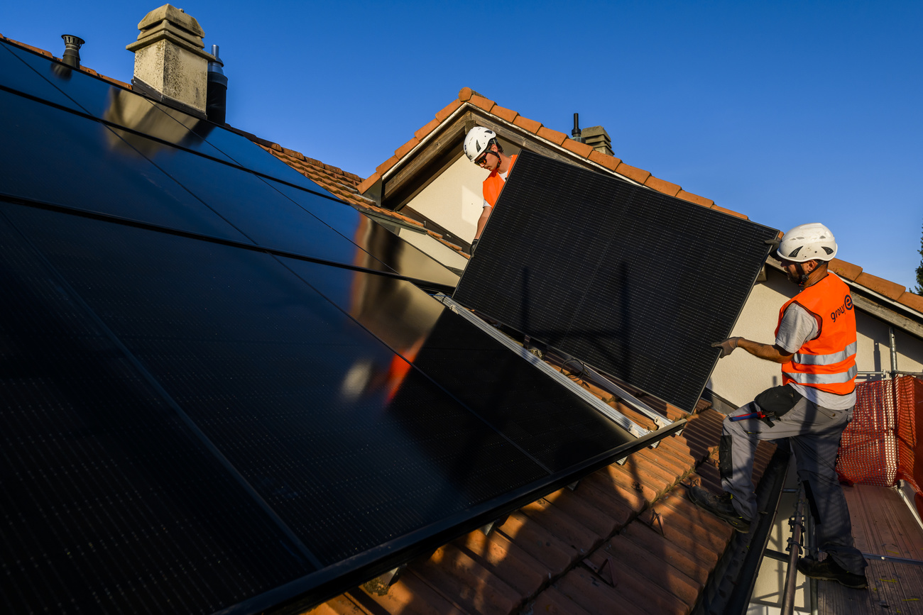 Workers set up solar panels on the roof of a building in Switzerland.