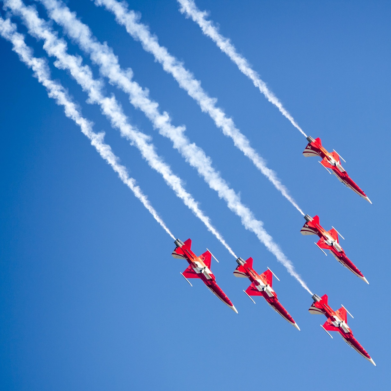 Fünf Flugzeuge der Patrouille Suisse fliegen durch einen blauen Himmel.