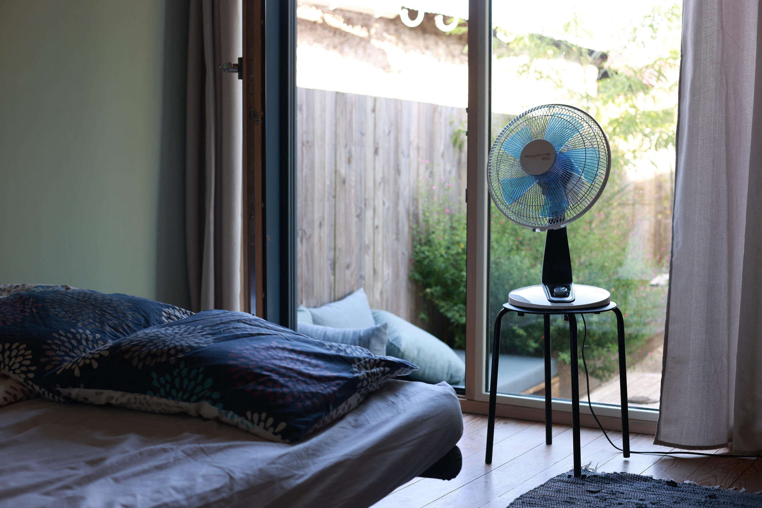 Schlafzimmer mit einem Ventilator auf einem Hocker am Bett