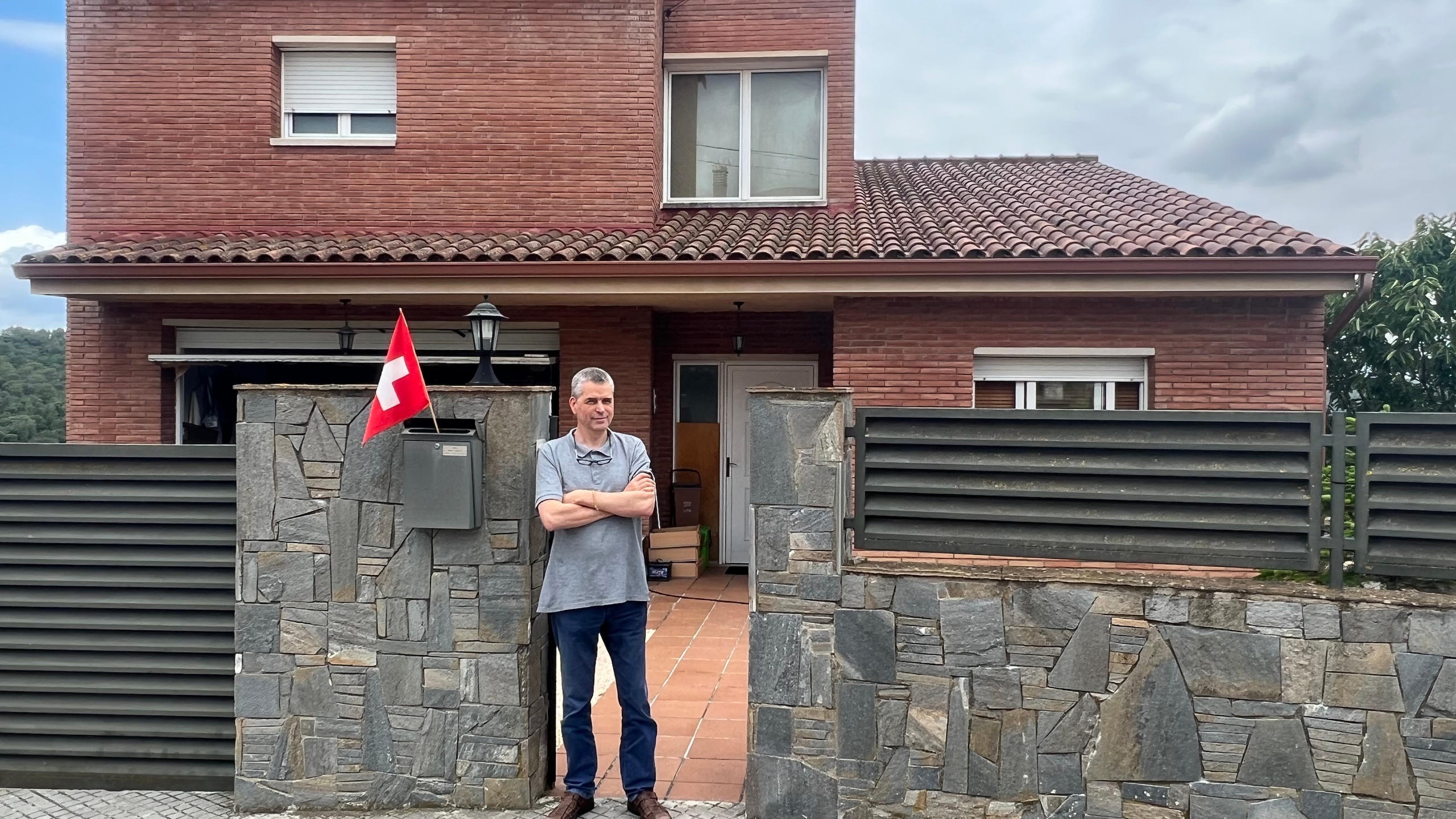 Mann steht neben einer Schweizerflagge vor einem Haus.