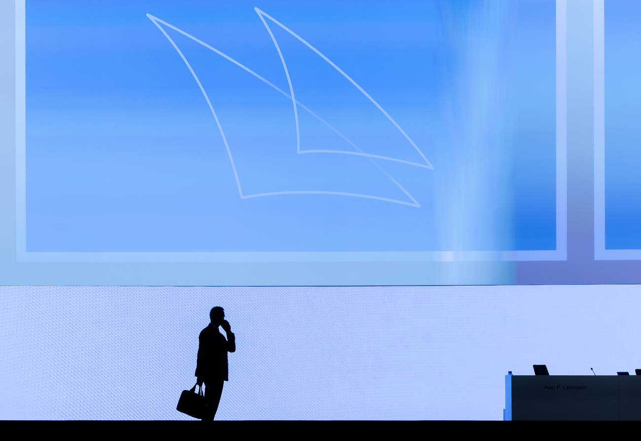 uomo con valigetta in mano partla al telefono, in piedi controluce sullo sfondo del logo di credit suisse
