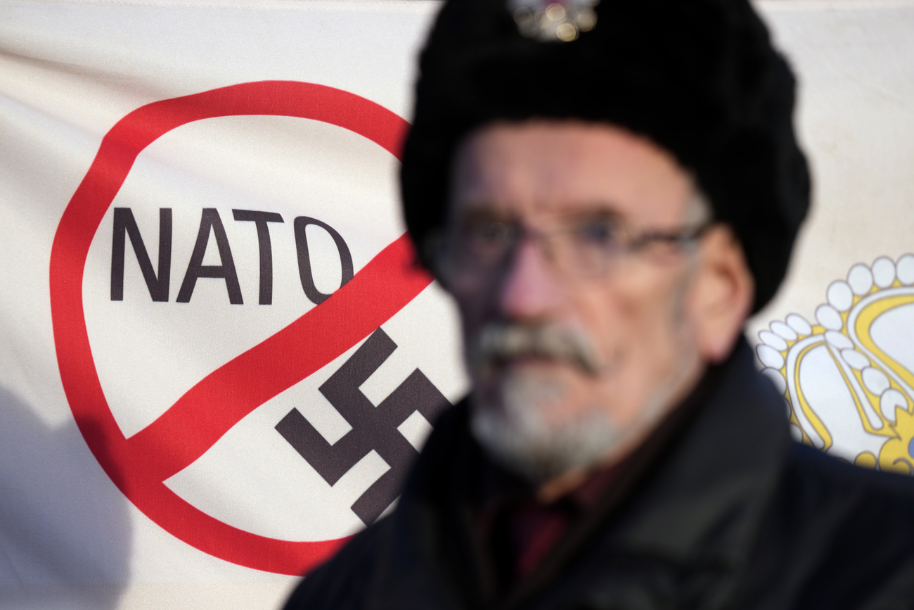 A man in front of a poster on which a swastika and a NATO banner are crossed out