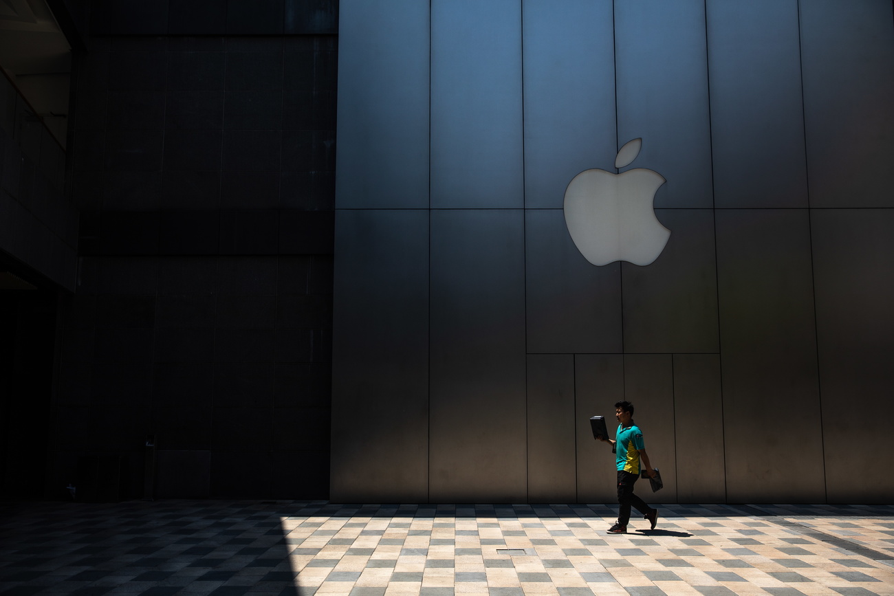 una persona cammina davanti al logo della mela di apple
