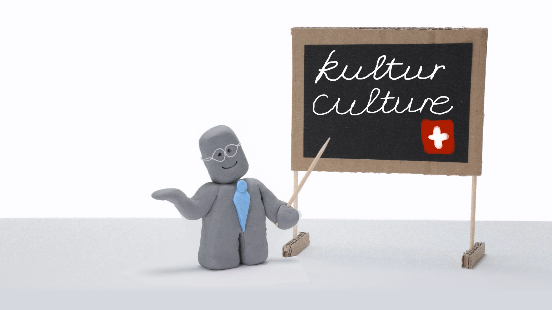 A plasticine person in front of a blackboard where it s written kultur/culture