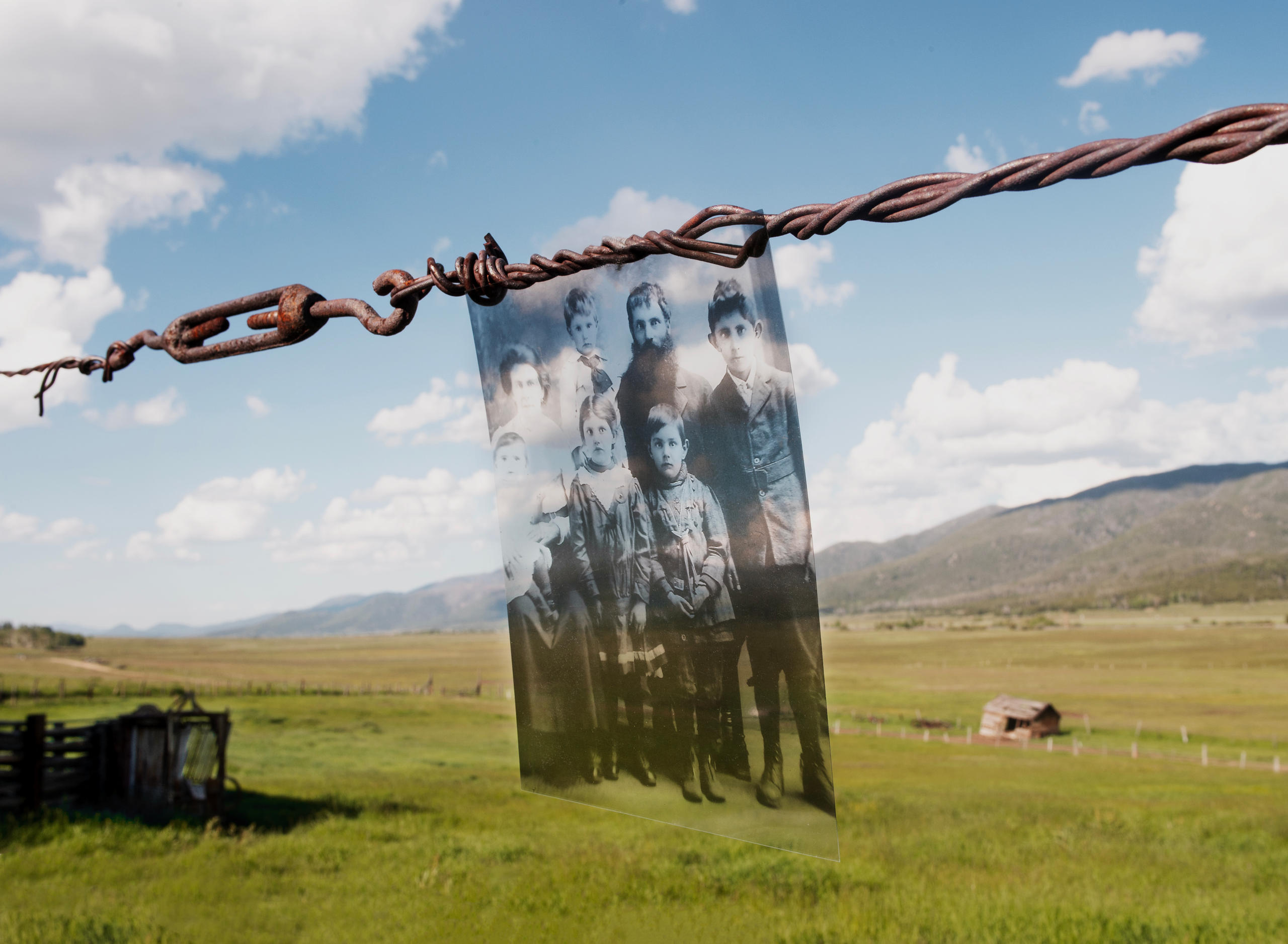 Photo of a photo hanging from barbed-wire, with a green landscape in the background.