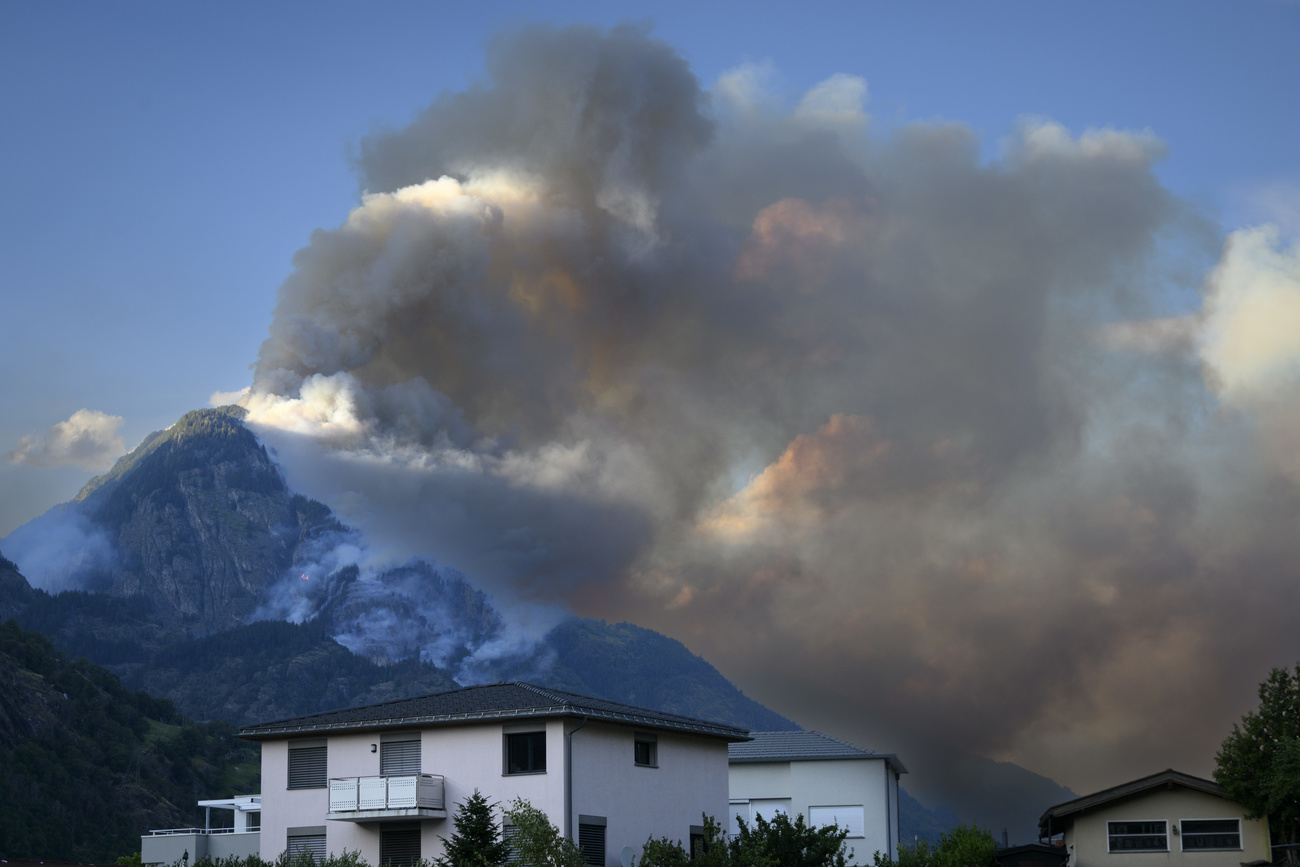 Im Vordergrund ein Haus, dahinter ein brennender Berg