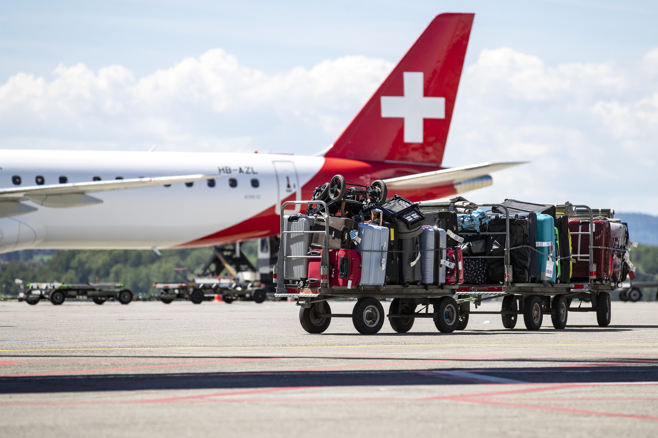 Gepäckwagen auf Flugpiste, im Hintergrund ein Flugzeug mit Schweizer Kreuz
