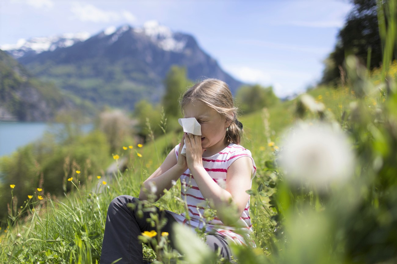 Una niña se suena la nariz en medio de un prado florecido.