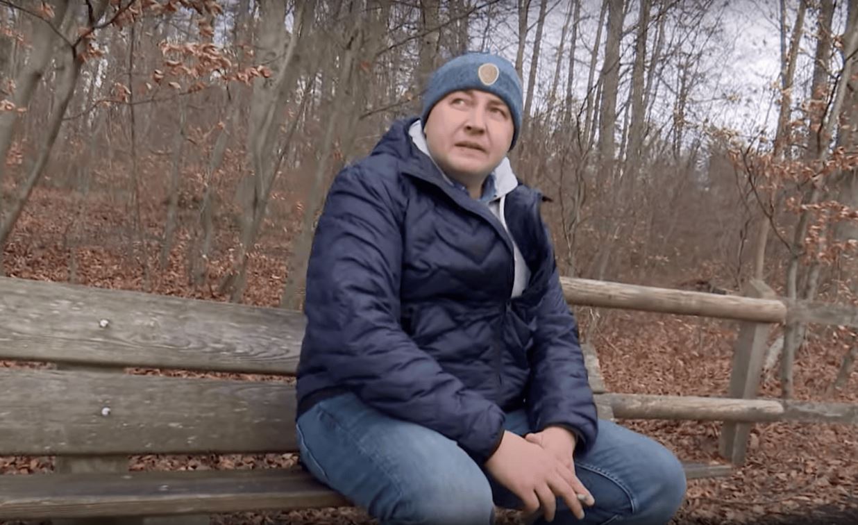 Mann auf einer Bank vor einem Wald