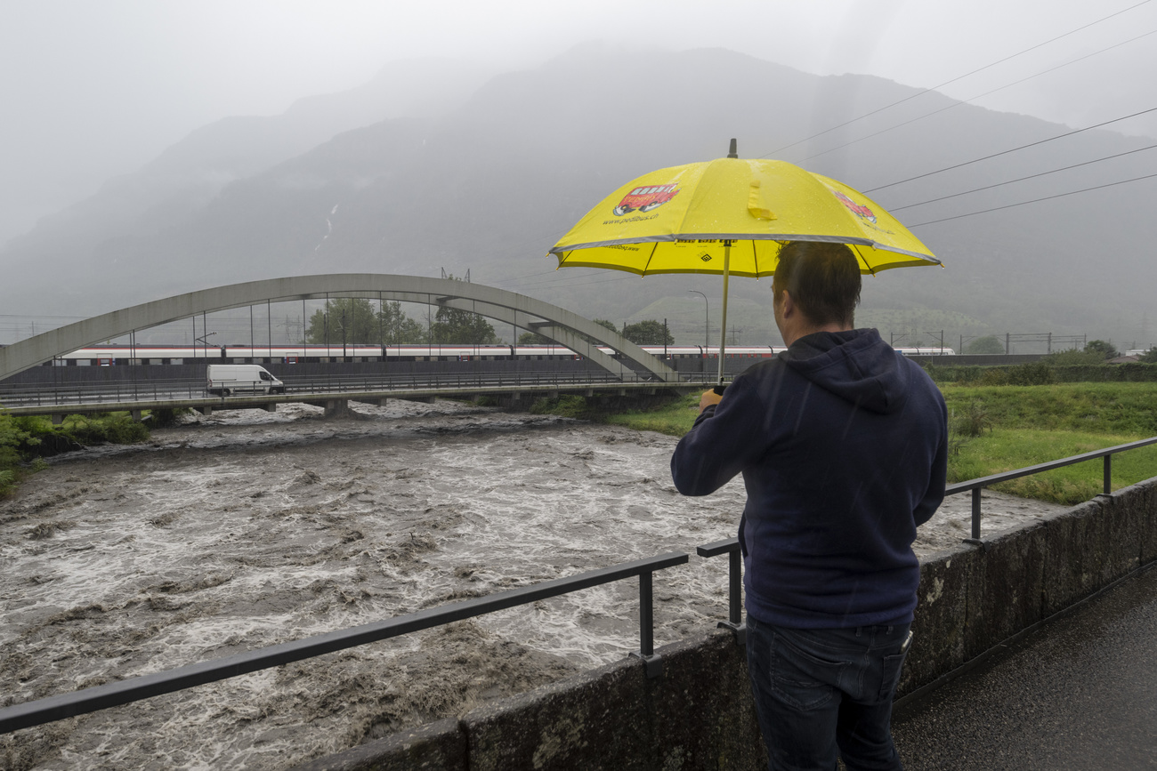 Mann mit Regenschirm schaut von einer Brücke auf einen Fluss mit braunem Hochwasser