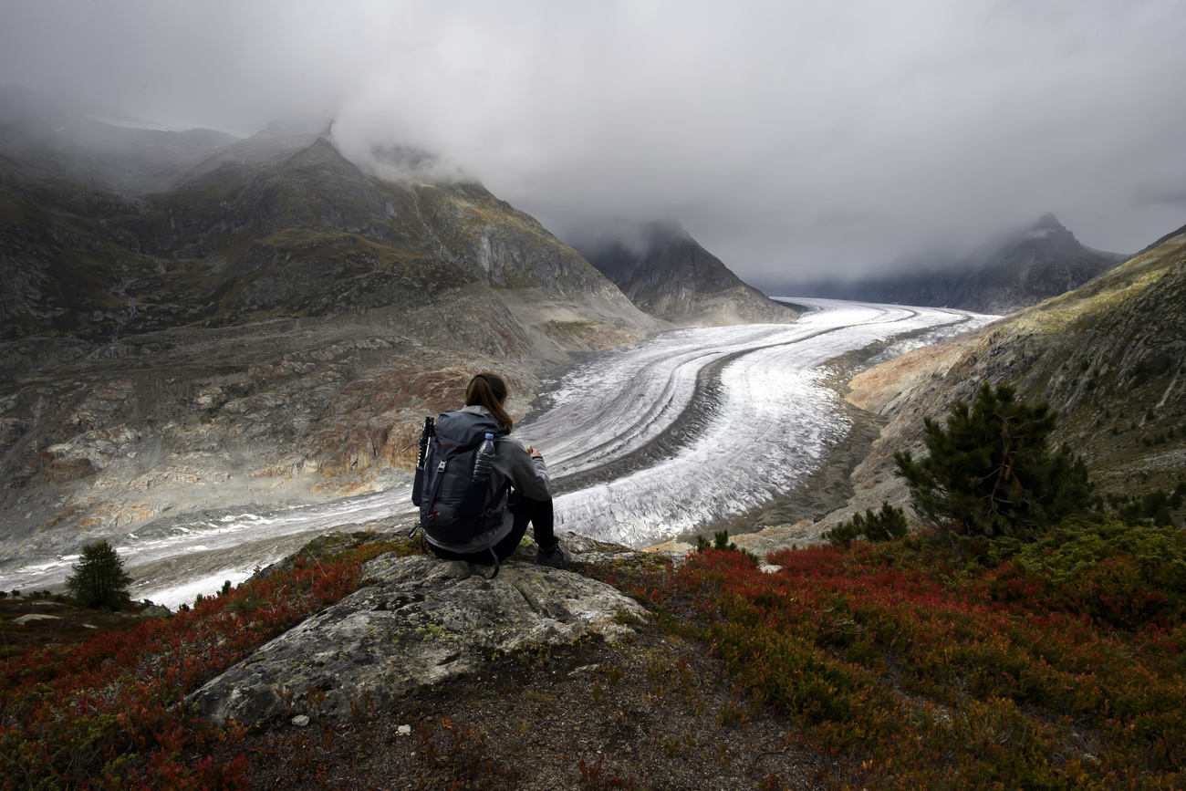 Eine Person, die auf einem Felsen vor einem Gletscher sitzt