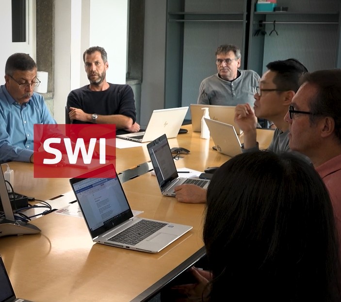 Einblick in eine Redaktionssitzung bei swissinfo (grosser Tisch, diverse Menschen, aufgeklappte Laptops)