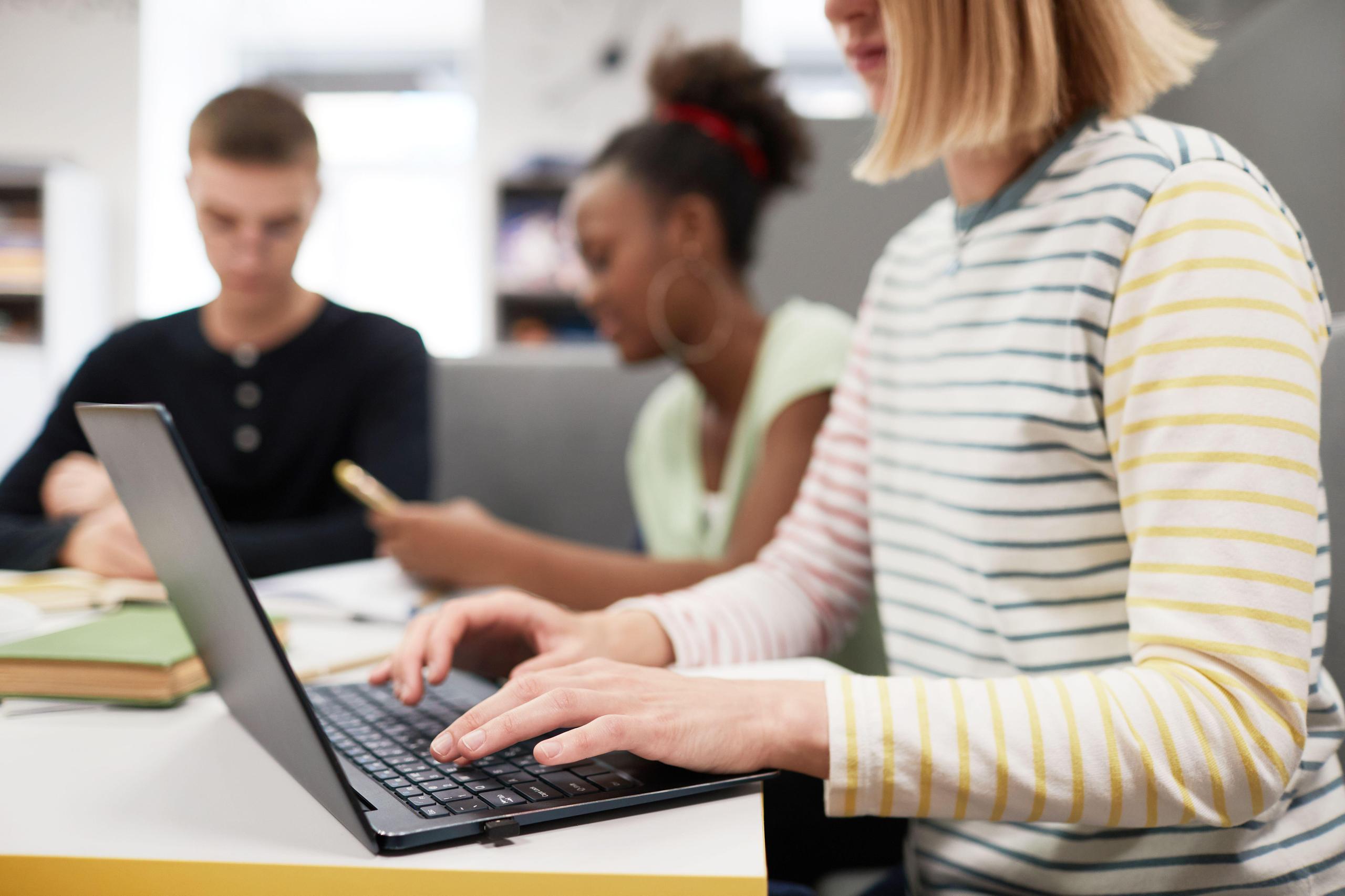A woman in the foreground working on a computer. Two persons work in the background