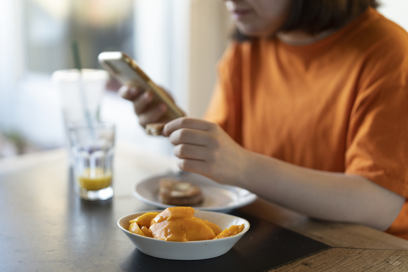 persona con telefono in mano mentre fa colazione