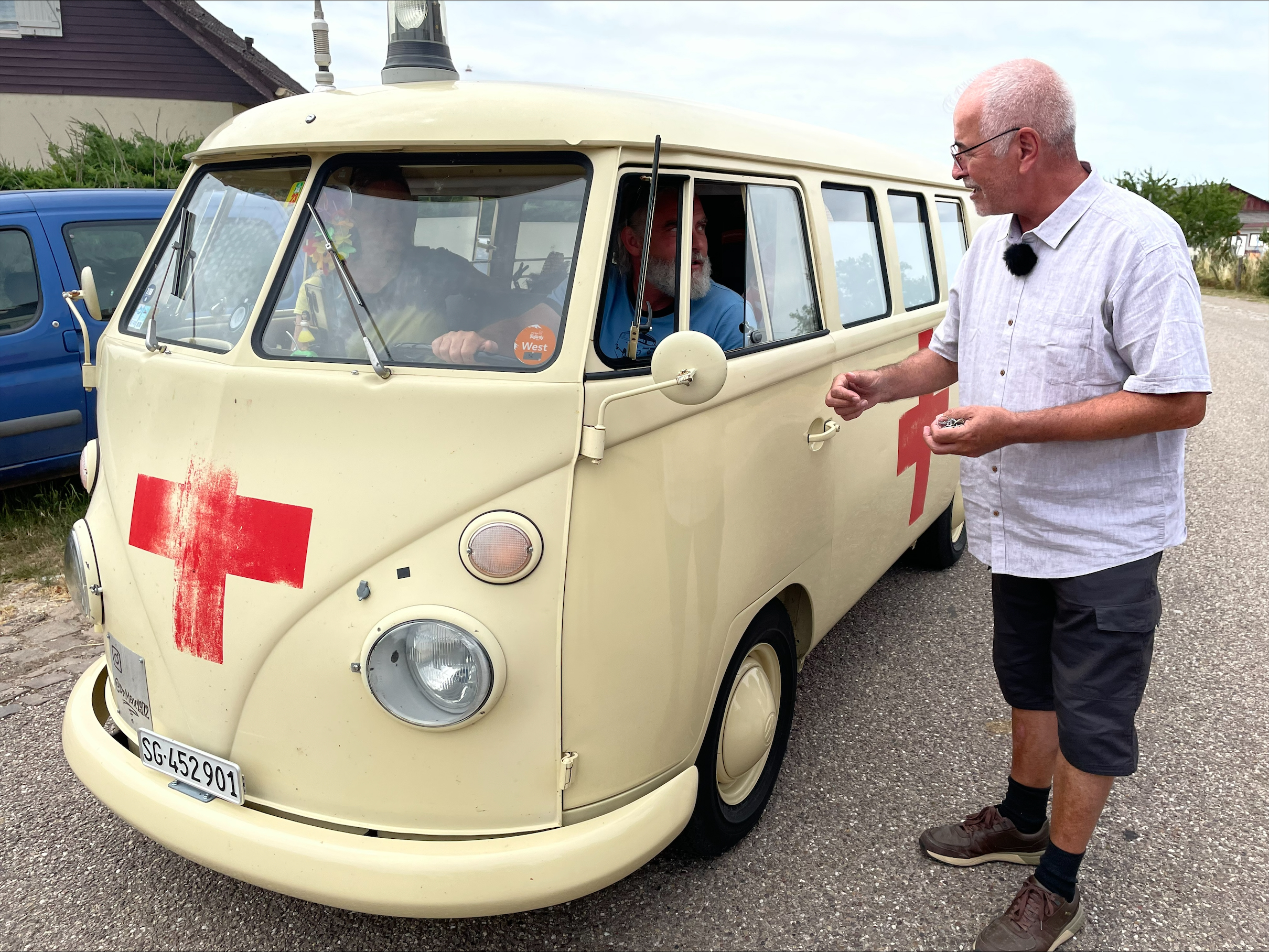 Couple in VW bus and man standing next to it