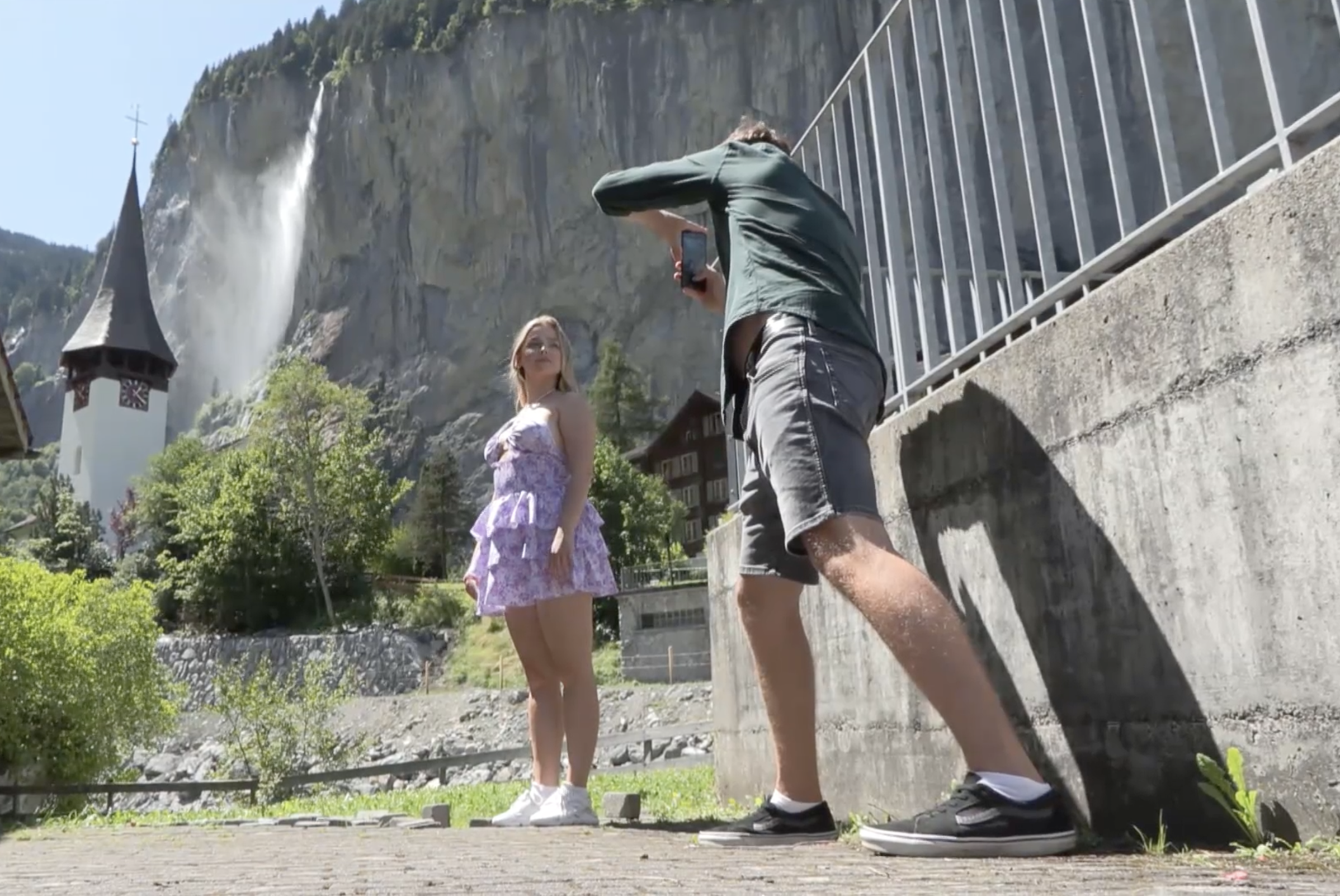 un ragazzo fotografa una ragazza davanti a un campanile e a una cascata