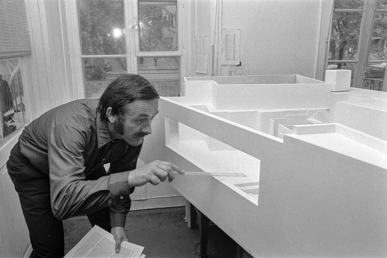 Homme accroupi devant une maquette de bâtiment