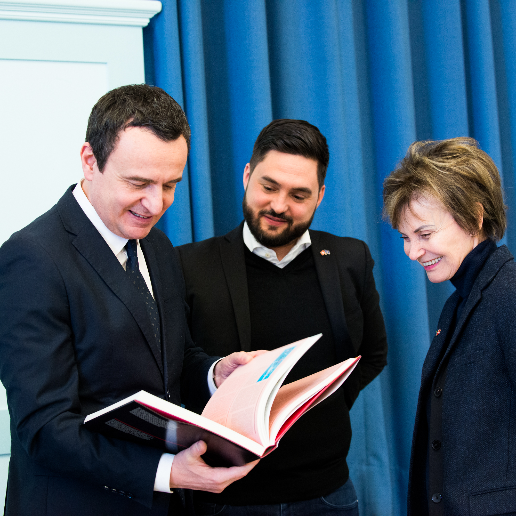 Three politicians look into a kind of guest book.